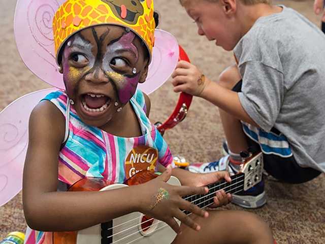 Child in costume playing guitar and singing.