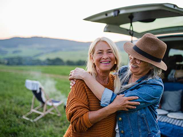 two middle aged women standing outside by their car and chairs